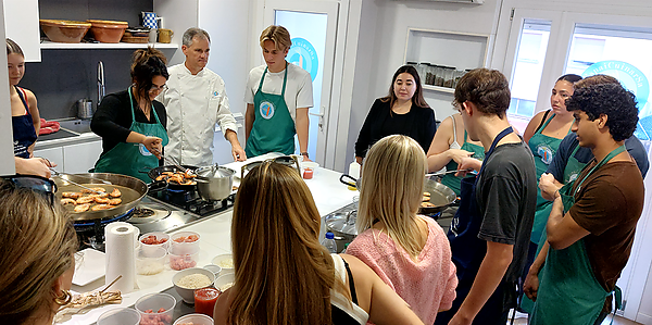 Turistes aprenent a fer paella amb ingredients frescos en una classe interactiva.